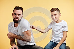 Bearded dad and his son playing and fighting over yellow background. boy beats father to shoulder while him fear