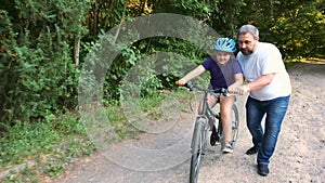Bearded dad teaches his daughter in a Bicycle helmet to ride a bike in the Park. The happy sport family