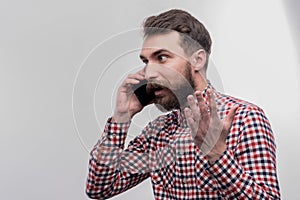 Bearded dark-haired man feeling angry while having phone conversation