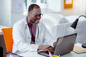 Bearded dark-skinned medical scientist working on laptop