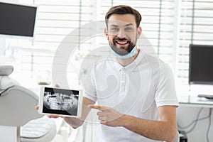 Bearded dentist showing x-ray on tablet screen in modern dental clinic