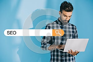 bearded developer using laptop on blue with SEO