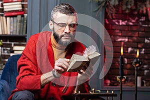 Bearded diviner sitting at the table with candles and enjoying self-education