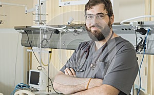 Bearded doctor wearing glasses and a gray robe works with hospital equipment