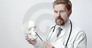 Bearded doctor in white lab with human skull