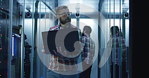 Bearded IT engineer using laptop in server room