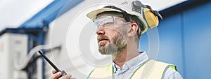 Bearded engineer wearing helmet using walkie-talkie to communicate with industry produce site photo