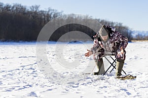 Bearded european man is boring while he fishing from ice hole