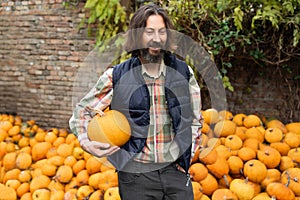 Bearded farmer with pumpkin on a background of a pile of pumpkins