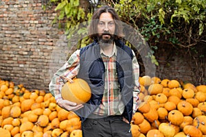 Bearded farmer with pumpkin on a background of a pile of pumpkins