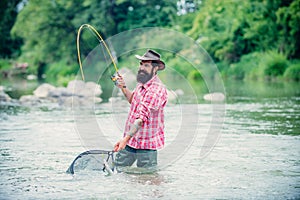 Bearded fisher in water. Young man fishing. Successful fly fishing. Fisher masculine hobby. Man with fishing rod and net