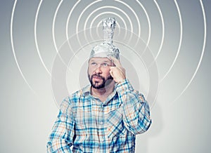 Bearded funny man in a cap of aluminum foil sends signals. Concept art phobias photo