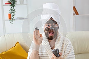 Bearded funny man having fun with a cosmetic mask on his face made from black clay. Men skin care, humor and spa at home