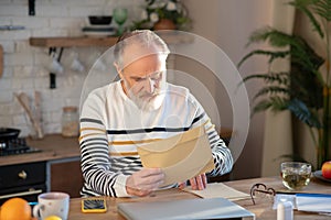Bearded grey-haired man sitting at the table with a newspapaer in his hands photo