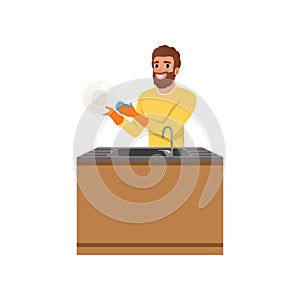 Bearded guy in orange rubber gloves washing plate with sponge. Young man doing household chores. Cleaning and