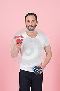 Bearded guy with red and blue hearts in hands. I prepared gift for you. Young man in white t-shirt holding gift boxes