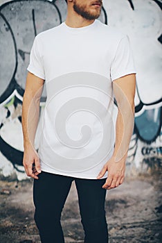 Bearded guy wearing white blank t-shirt and black jeans, standing opposite garage. Vertical