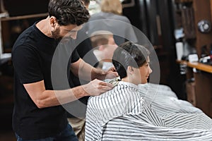 Bearded hairdresser trimming hair of teen