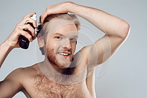Bearded hairy man sprinkles lotion on hair.