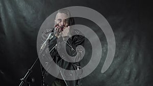 Bearded hairy rock musician in leather jacket blows a kiss, holding fists up and leaves the stage on concert with black