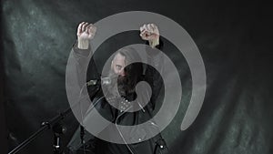 Bearded hairy rock musician in leather jacket smiles, blows a kiss, holding fist up and leaves the stage on concert with