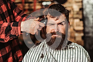 Bearded handsome man visiting hairstylist. Barber shop. Barber shearing beard to man. Male hairstylist serving client