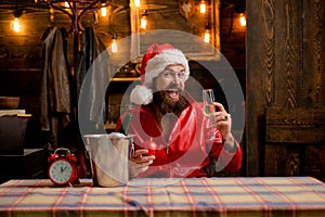 Bearded handsome Santa Claus smile and drink champagne. Christmas lights garland. Santa waiting for New Year midnight