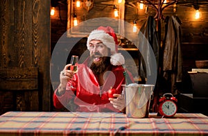 Bearded handsome Santa Claus smile and drink champagne. Christmas lights garland. Santa waiting for New Year midnight