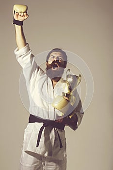 Bearded happy karate man in kimono, boxing gloves, champion cup