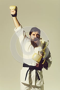 Bearded happy karate man in kimono, boxing gloves, champion cup