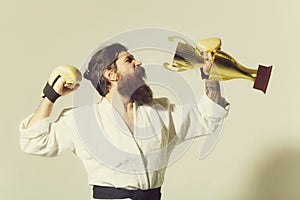 Bearded happy karate man in kimono, boxing gloves, champion cup