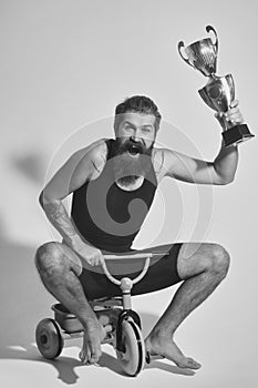 Bearded happy man holds gold champion cup on bicycle toy