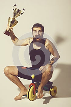 Bearded happy man holds gold champion cup on bicycle toy