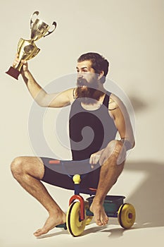 Bearded happy man holds gold champion cup on bicycle toy