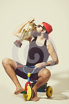 Bearded happy man kissing gold champion cup on bicycle toy