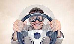 Bearded happy man in stylish goggles with steering wheel on background, car driver concept