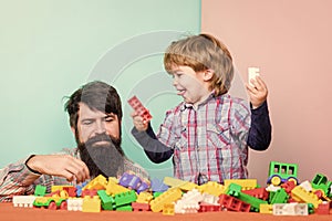 Bearded hipster and boy play together. Dad and child build plastic blocks. Child care concept. Happy family. Child