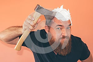 Bearded hipster man shaving his head with an axe