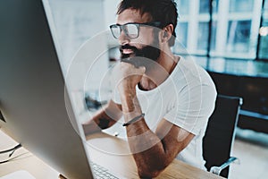 Bearded hipster professional wearing eye glasses working at modern loft studio-office with desktop computer.Panoramic