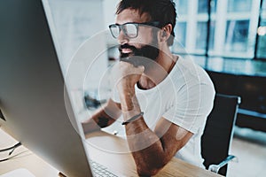 Bearded hipster professional wearing eye glasses working at modern loft studio-office with desktop computer.Panoramic photo