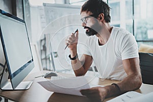 Bearded hipster professional wearing eye glasses working at modern loft studio-office with desktop computer.White blank