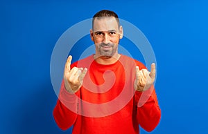 Bearded hispanic man in his 40s wearing a red sweatshirt making a rock gesture in concept of rebellion and illegality