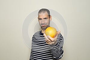 Bearded Hispanic man in his 40s wearing a striped sweater offering you an orange isolated on beige background. Healthy