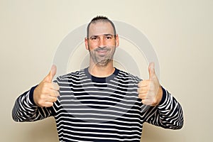 Bearded Hispanic man in his 40s wearing a striped sweater with thumbs up giving thumbs up to seaweed, isolated on beige