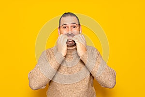 Bearded hispanic man wearing beige turtleneck biting his nails terrified of traumatic situation, feeling panic when