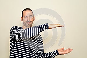 Bearded Hispanic man wearing a striped sweater with his arms open in profile offering something while smiling at the