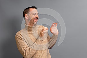Bearded hispanic man wearing a turtleneck pulled to the side with his hands in front in a gesture of embarrassment and