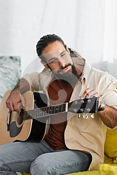 bearded hispanic musician tunning acoustic guitar