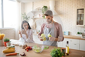 Bearded husband taking lettuce while cooking salad for wife