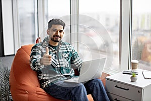 Bearded indian man showing thumb up with laptop on knees